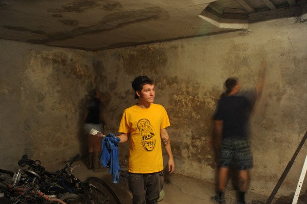Re Mić considers what to paint next while Tamina and Tameo work on re-plastering the walls of the Center's basement.